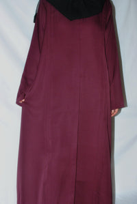 Back view of a dark maroon abaya with long sleeves and black headscarf on plain background