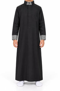 Boy wearing a black Saudi thobe with black and white patterned collar and cuffs, front view
