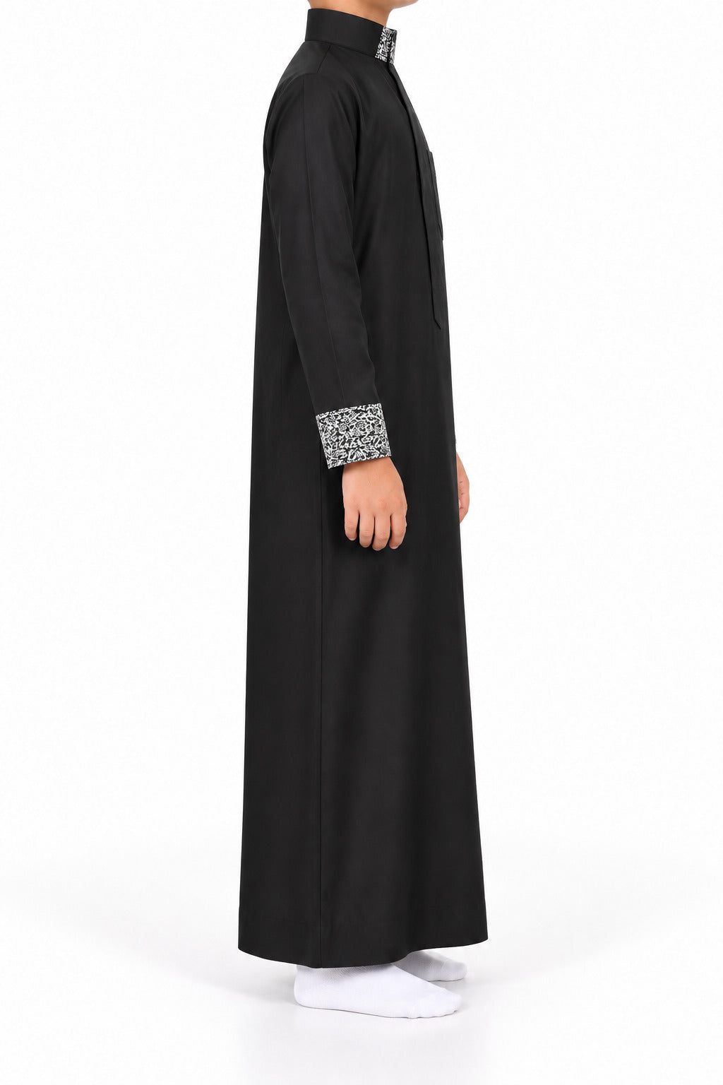 Side view of a boy wearing a black Saudi thobe with black and white patterned collar and cuffs
