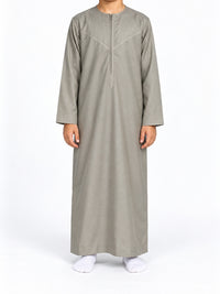 Boy wearing a cement grey Omani thobe with curved chest stitching, front view