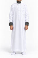 Boy wearing a white Saudi thobe with black and white patterned collar and cuffs, front view