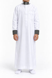 Boy wearing a white Saudi thobe with black and white patterned collar and cuffs, front view