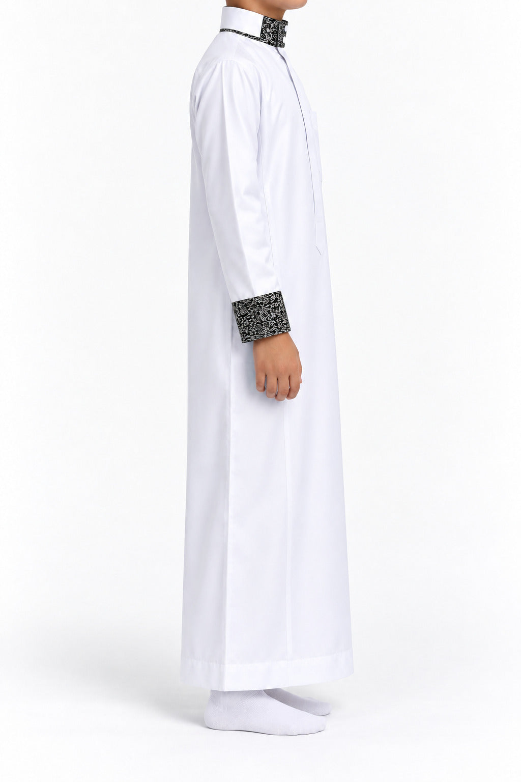 Side view of a boy wearing a white Saudi thobe with black and white patterned collar and cuffs