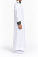 Side view of a boy wearing a white Saudi thobe with black and white patterned collar and cuffs