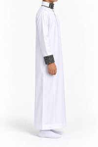 Side view of a boy wearing a white Saudi thobe with black and white patterned collar and cuffs