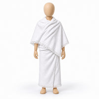 White two-piece children’s ihram with fringed edges displayed on a wooden child-sized mannequin